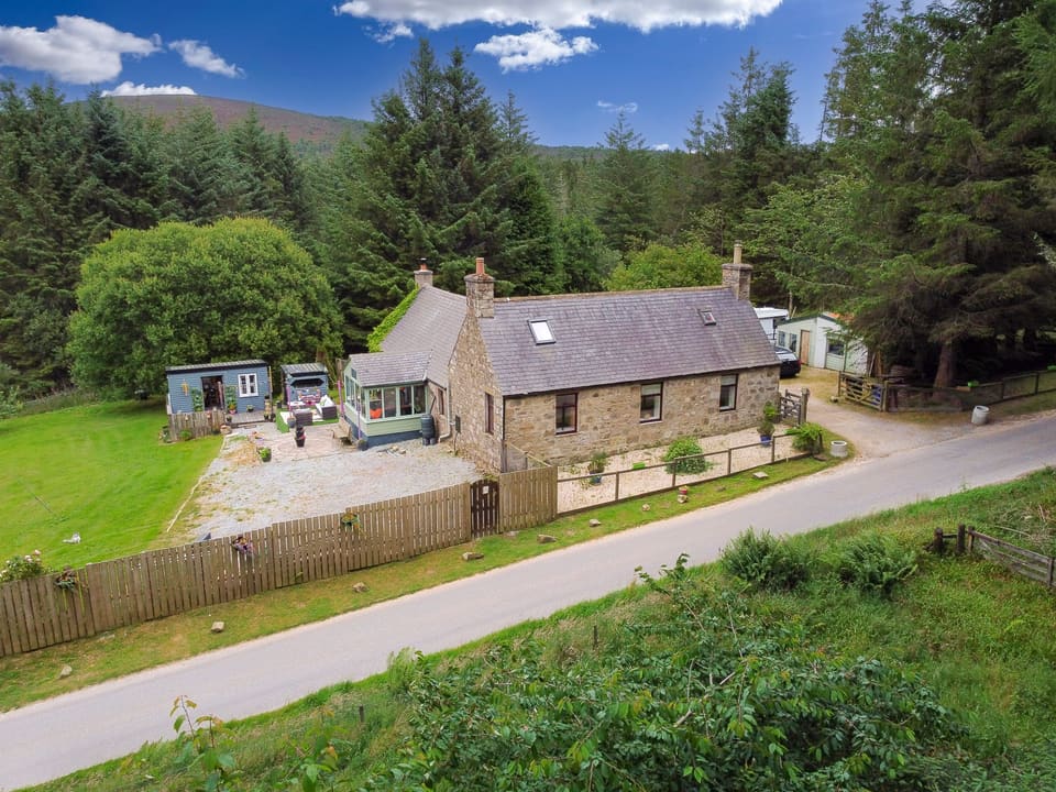 Stone cottage and garden from above, with woodland behind